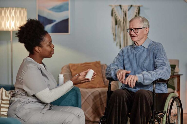 An older adult sits at a kitchen table reviewing monthly bills and budgeting paperwork with a family member.